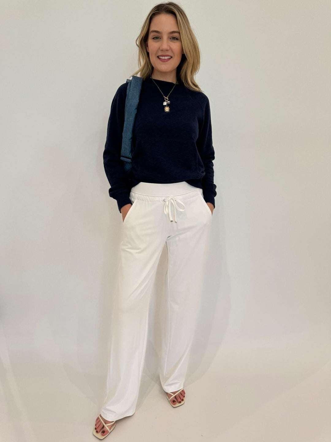 BK Fiona Crew Neck Sweatshirt in Dark Night paired with Raffaello Rossi Candice Straight Pants in White, Mignonne Gavigan Delancey Charm Necklace, Vee Collective Porter Messenger Bag in Denim - all available at Barbara Katz