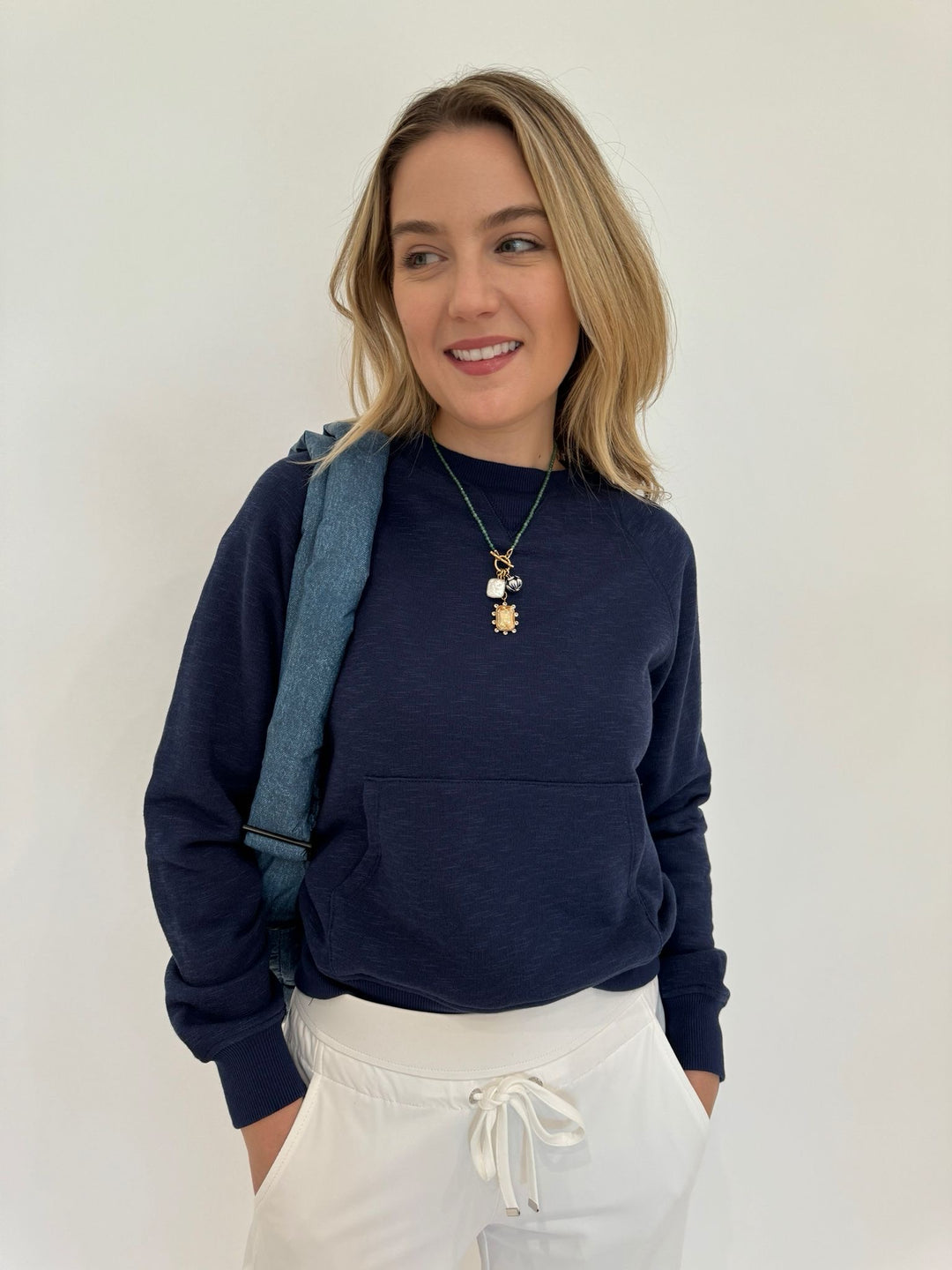 BK Fiona Crew Neck Sweatshirt in Dark Night paired with Raffaello Rossi Candice Straight Pants in White, Mignonne Gavigan Delancey Charm Necklace, Vee Collective Porter Messenger Bag in Denim - all available at Barbara Katz