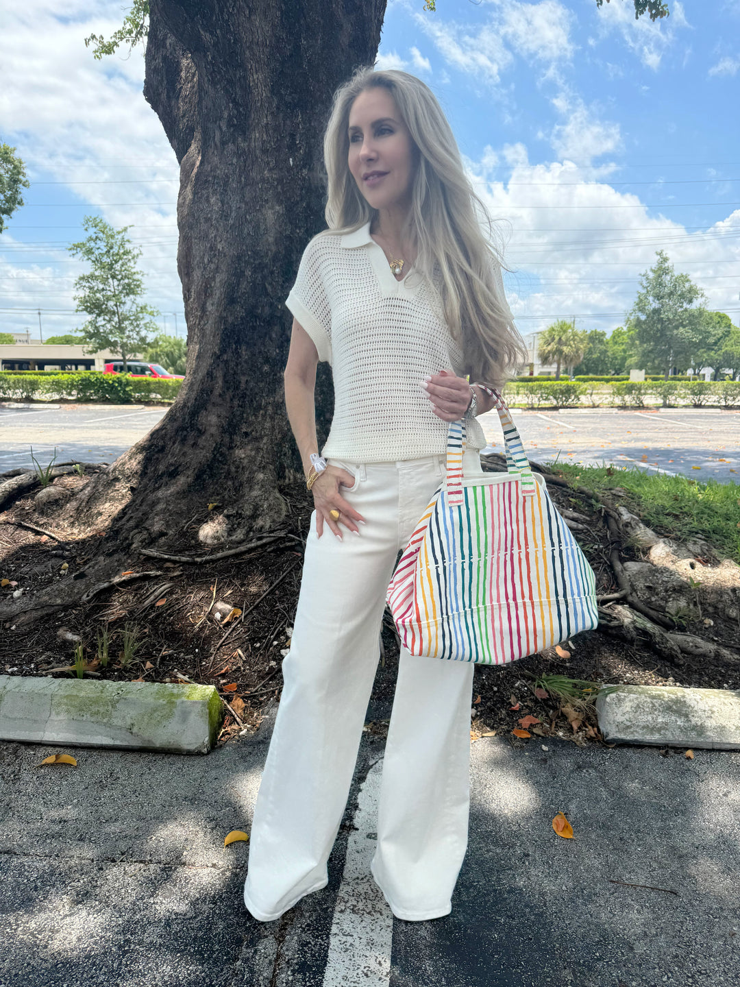 Model wearing Varley Otto Knit Vest in Egret and Mother The Twister Skimp Jeans, with Kerri Rosenthal Beach Stripes Tote Bag