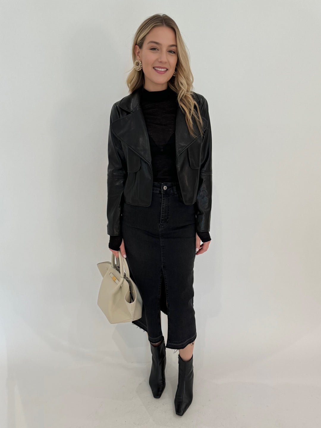 Adroit Atelier Ninon Vegan Leather Jacket in Black with Aldomartins Black Norin Top underneath, paired with Elliott Lauren Geneva Jean Midi Skirt, bag DeMellier The New York Midi Tote in Off White, all available at Barbara Katz